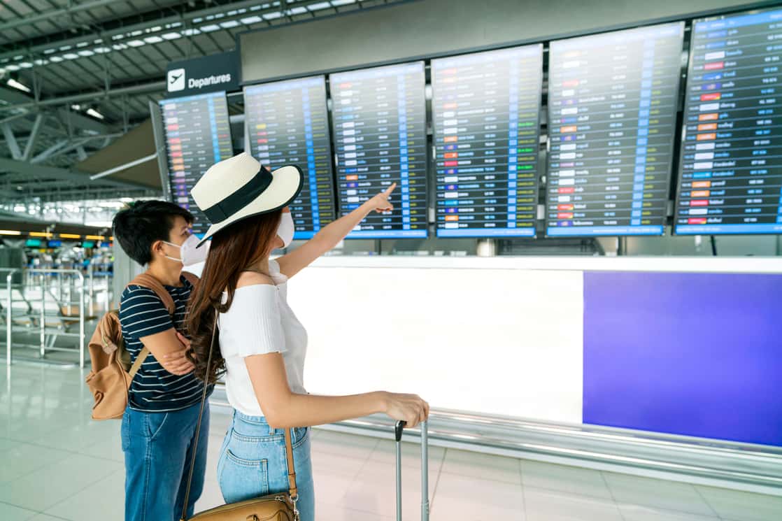 Two travelers pointing at a flight information board near an airport security checkpoint