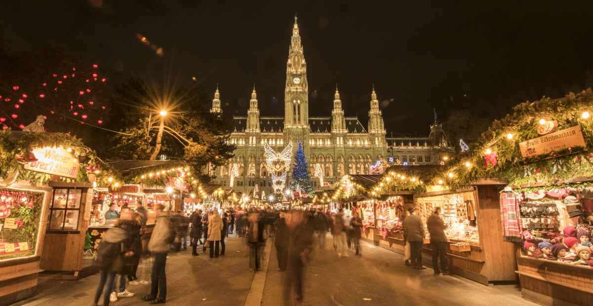 The Vienna Christmas Market in Austria, with festive stalls, a glowing Christmas tree, and the historic Rathaus in the background.