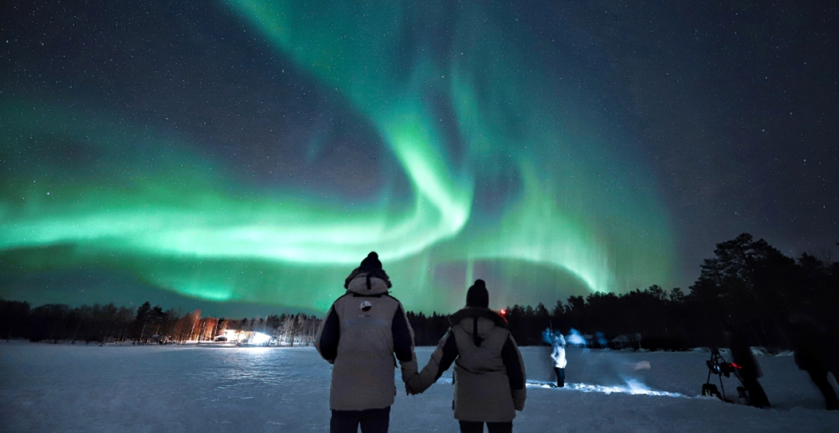 Couple holding hands under the Northern Lights in Lapland's snowy wilderness.