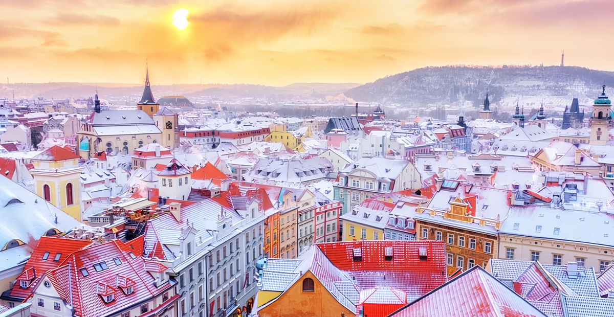 Snow-covered rooftops of Prague during a golden winter sunset.